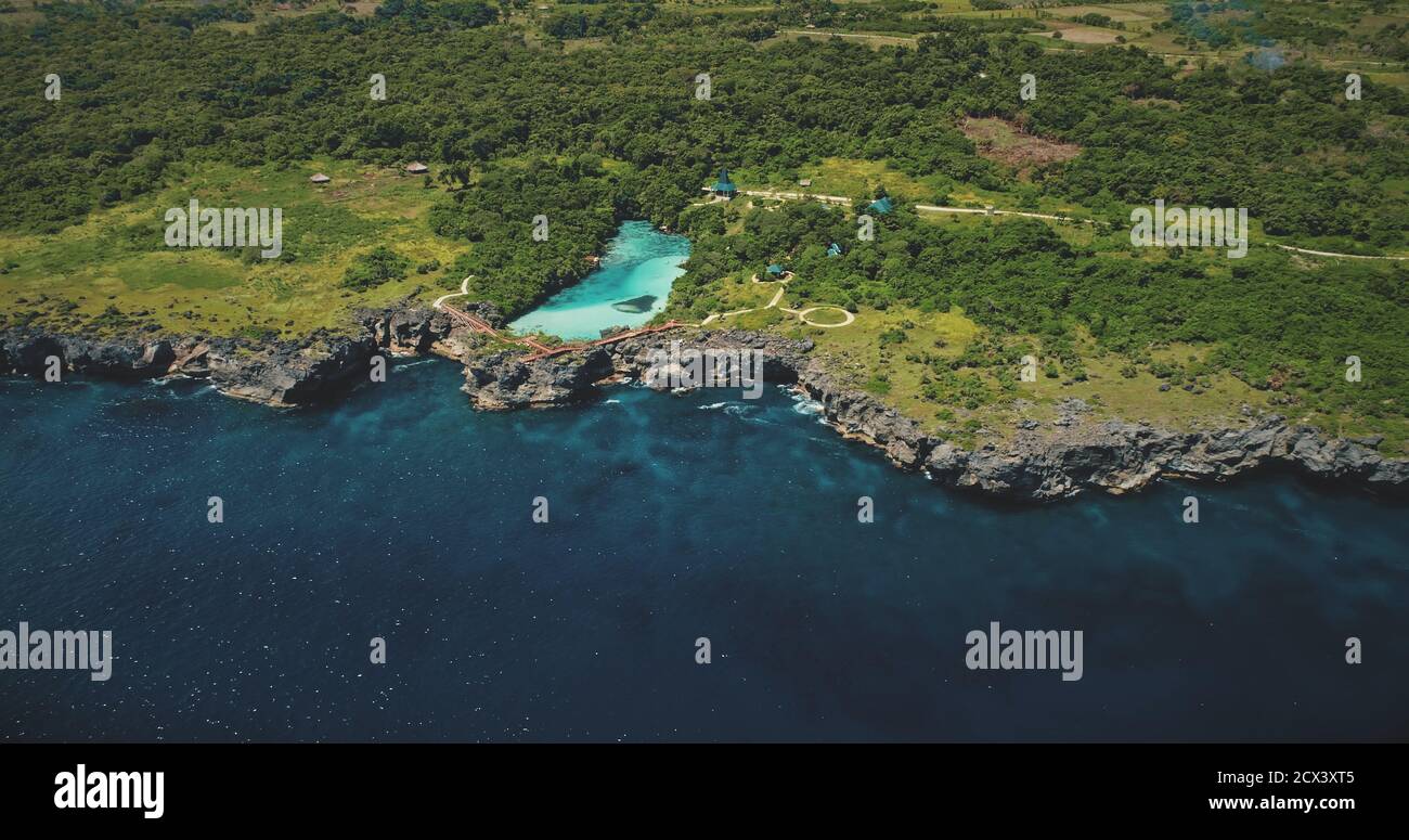 Azure lake on green rock coast at sea bay in aerial view. Tropical nature landscape of Sumba island, Indonesia. Beautiful salt water lagoon in greenery of trees and plants on cliffy sea shore Stock Photo