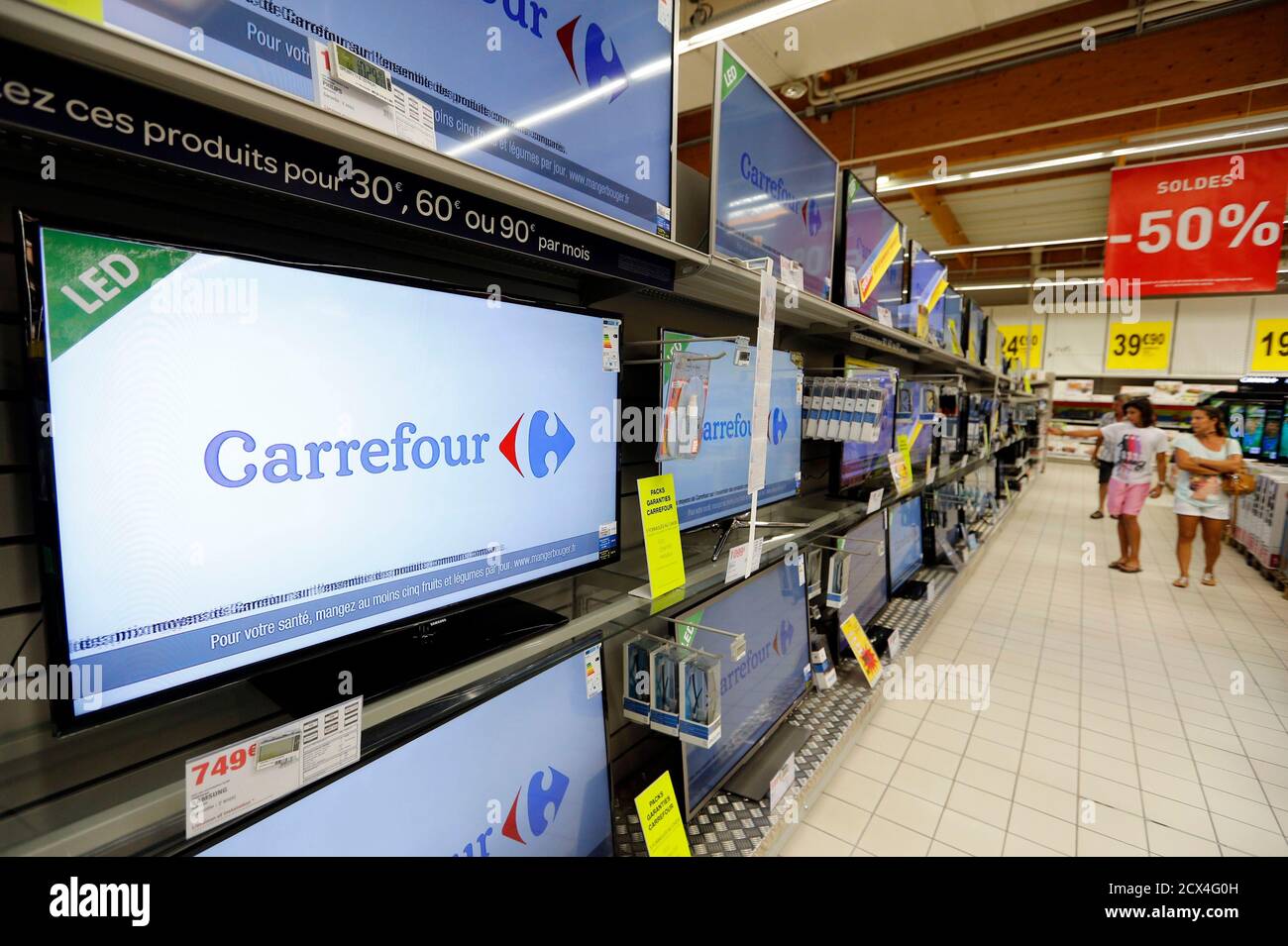 Customers look at television screens as they shop in a aisle at a Carrefour  hypermarket in Brive-La-Gaillarde, central France, July 8, 2013. France is  the biggest country in Europe for hypermarkets and