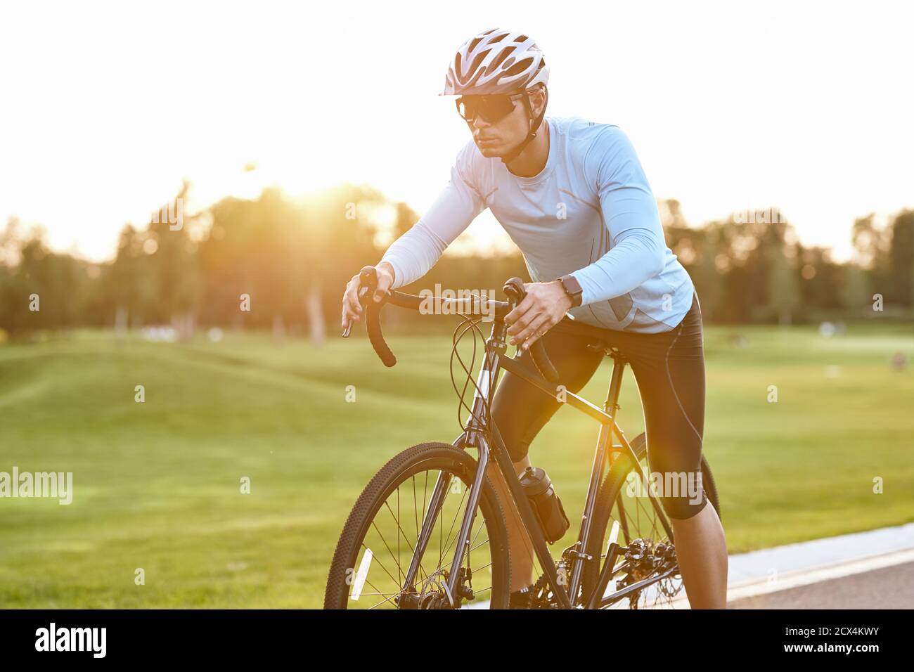 Professional road bicycle racer in sportswear and protective helmet standing on the road at sunset, ready to ride. Man cycling in the park. Active lifestyle and sport Stock Photo