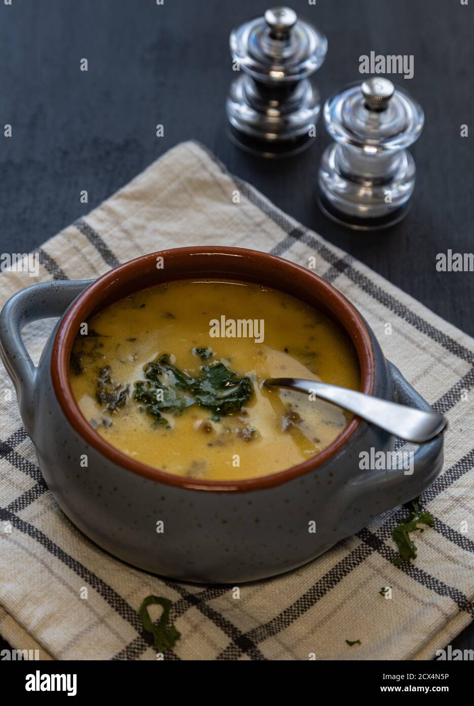 High angle shot of a potato, sausage and kale soup in a blue and orange bowl on a dish towel against a dark blue background. Stock Photo