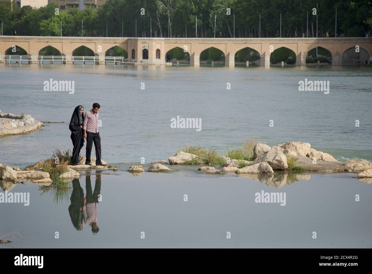 Iranian couple crossing stepping stones on the river Zayandeh, Isfahan, Iran Stock Photo