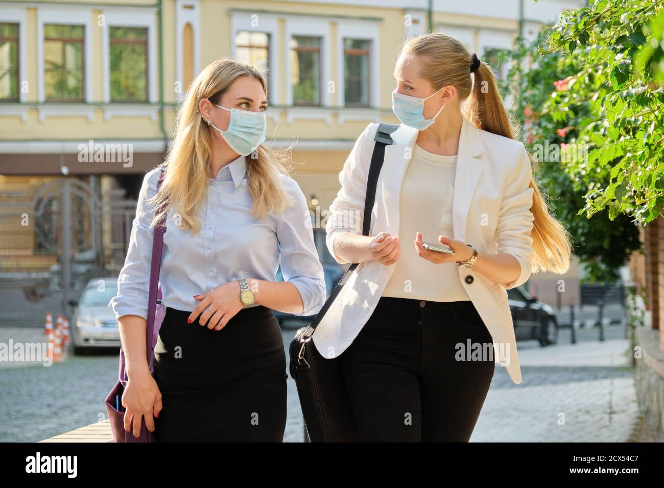 Office workers two women walking, wearing medical protective masks ...