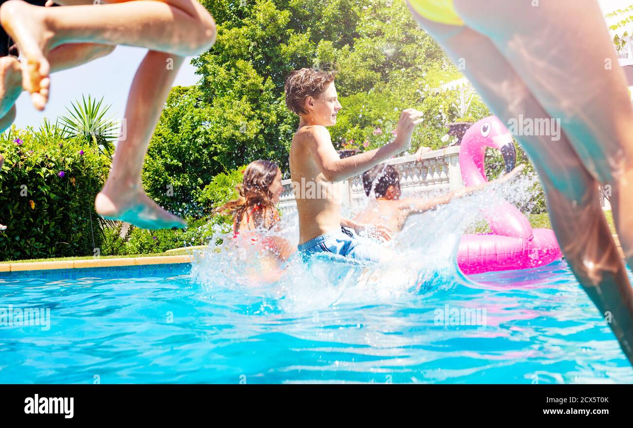 Boy in a group of friends jump into water pool together splashing down