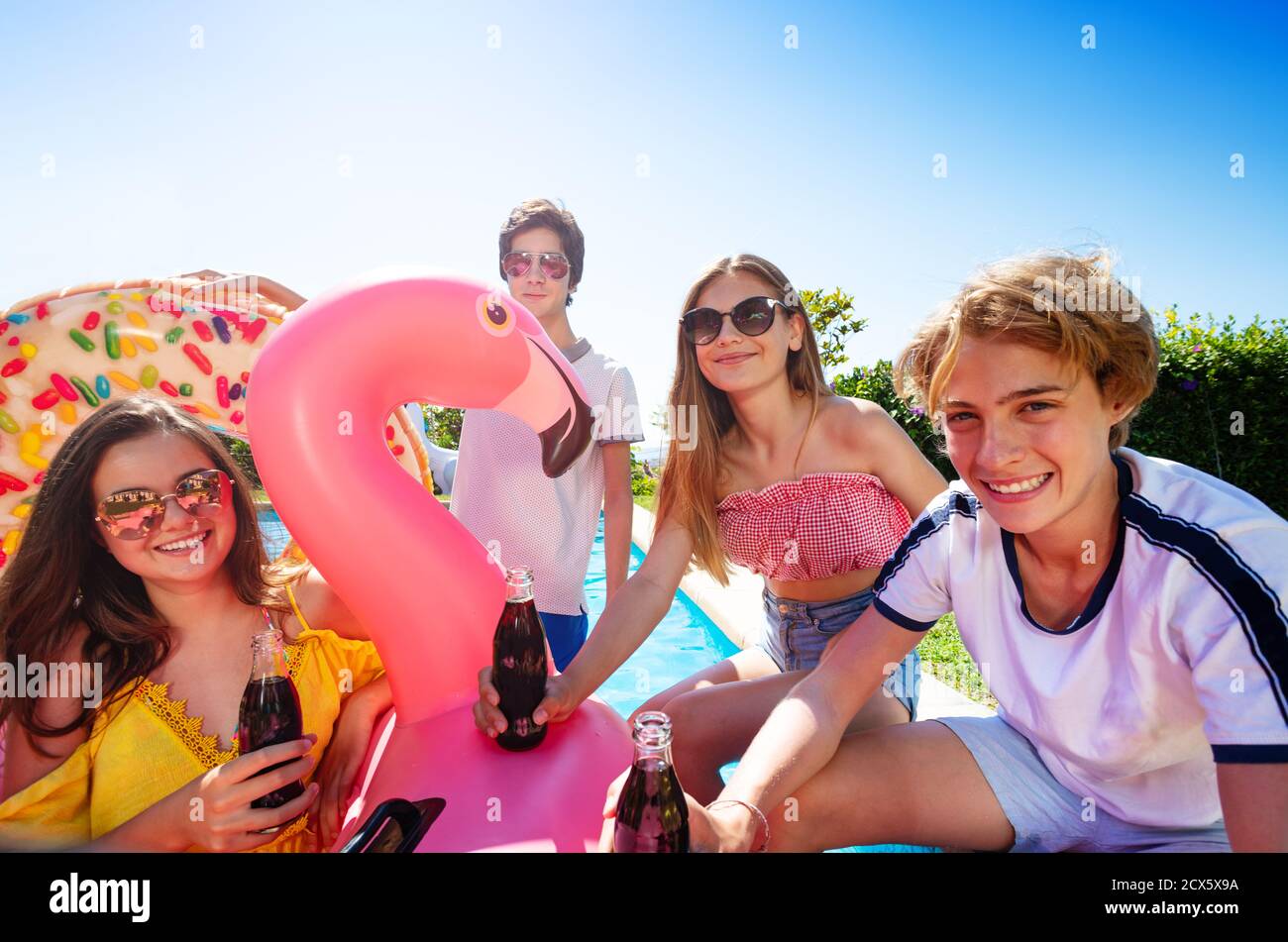 Teenage boys and girls chat, drink soda celebrating sitting on the border pool with inflatable buoys Stock Photo