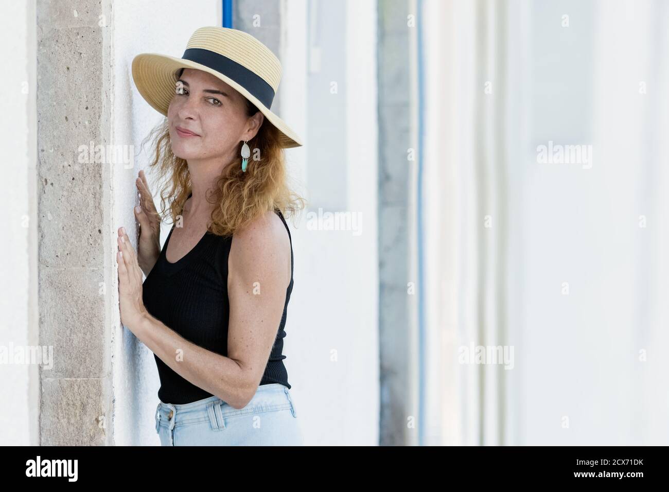 Portrait of a woman 40-45 years looking camera wearing casual clothes and a straw hat, serious, laying on a wall. Stock Photo