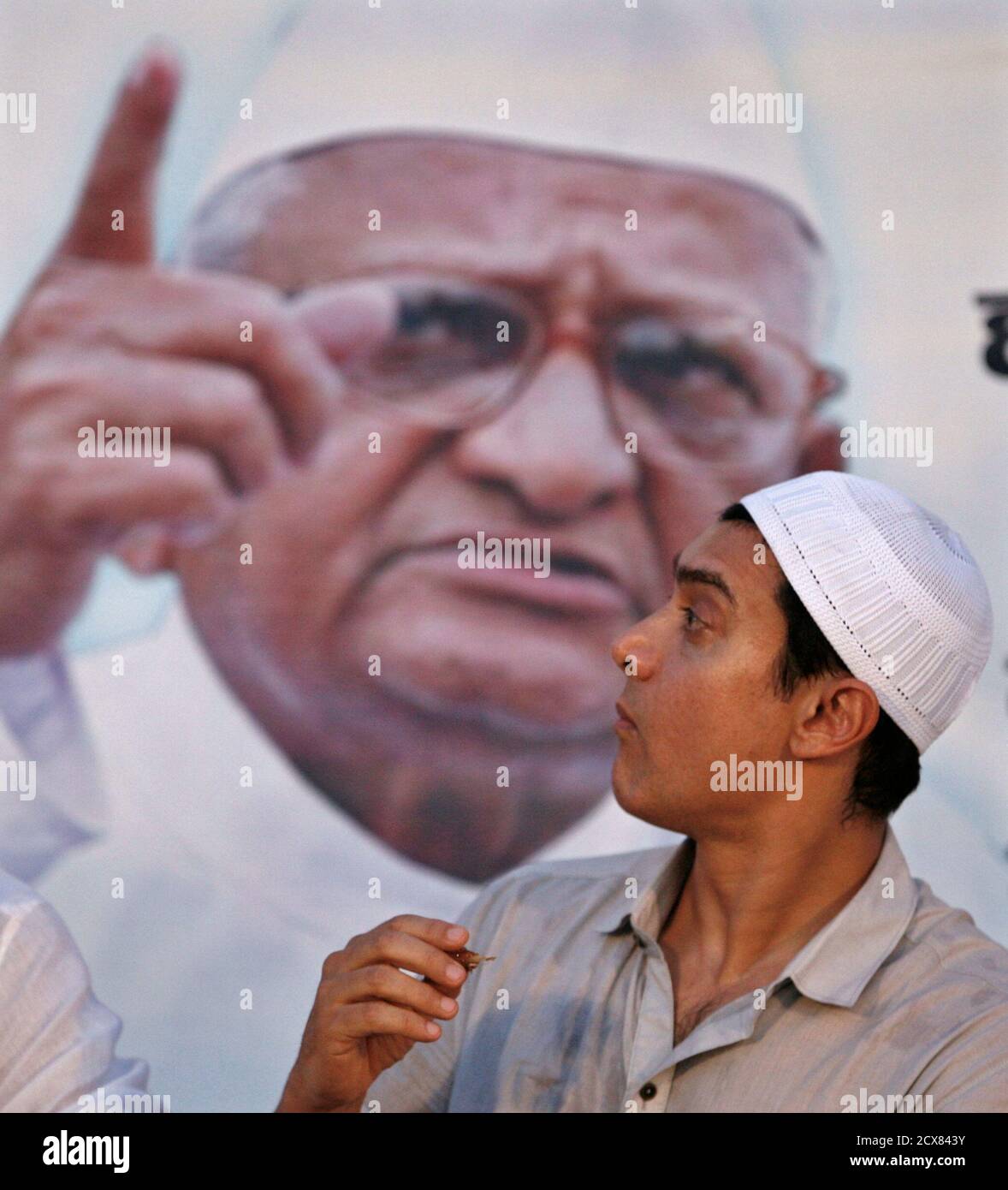 Bollywood actor Aamir Khan eats during Iftar, the evening meal for breaking fast, during the holy month of Ramadan, in front of a portrait of veteran Indian social activist Anna Hazare at Ramlila grounds where Hazare is fasting in New Delhi August 27, 2011. India's parliament edged closer to an agreement on Saturday on an anti-corruption bill that could end a 12-day hunger strike by a social activist that has lead to widespread anger against Prime Minister Manmohan Singh's besieged government. The campaign to get the legislation passed by 74-year-old Anna Hazare has struck a chord with million Stock Photo