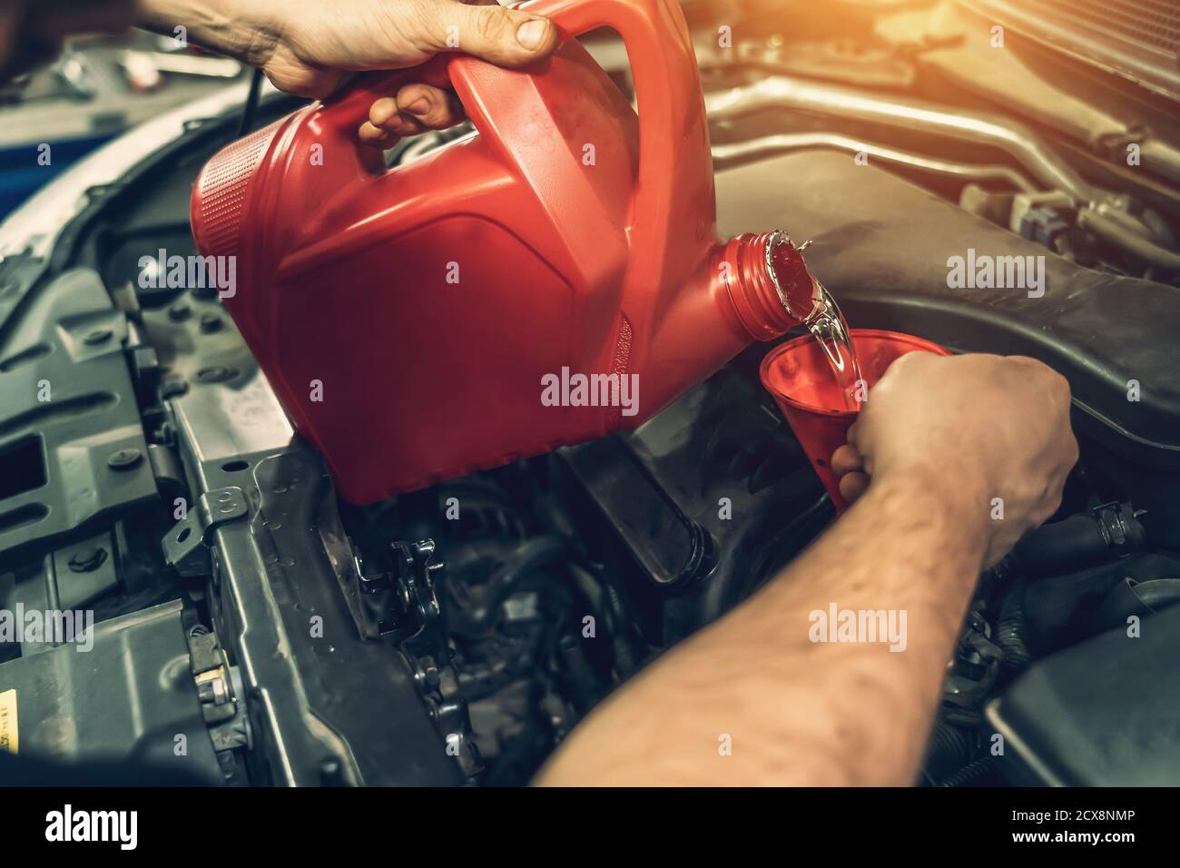 Worker hands pours flushing engine oil into engine to remove carbon deposits in auto service, correct timing change in car Stock Photo