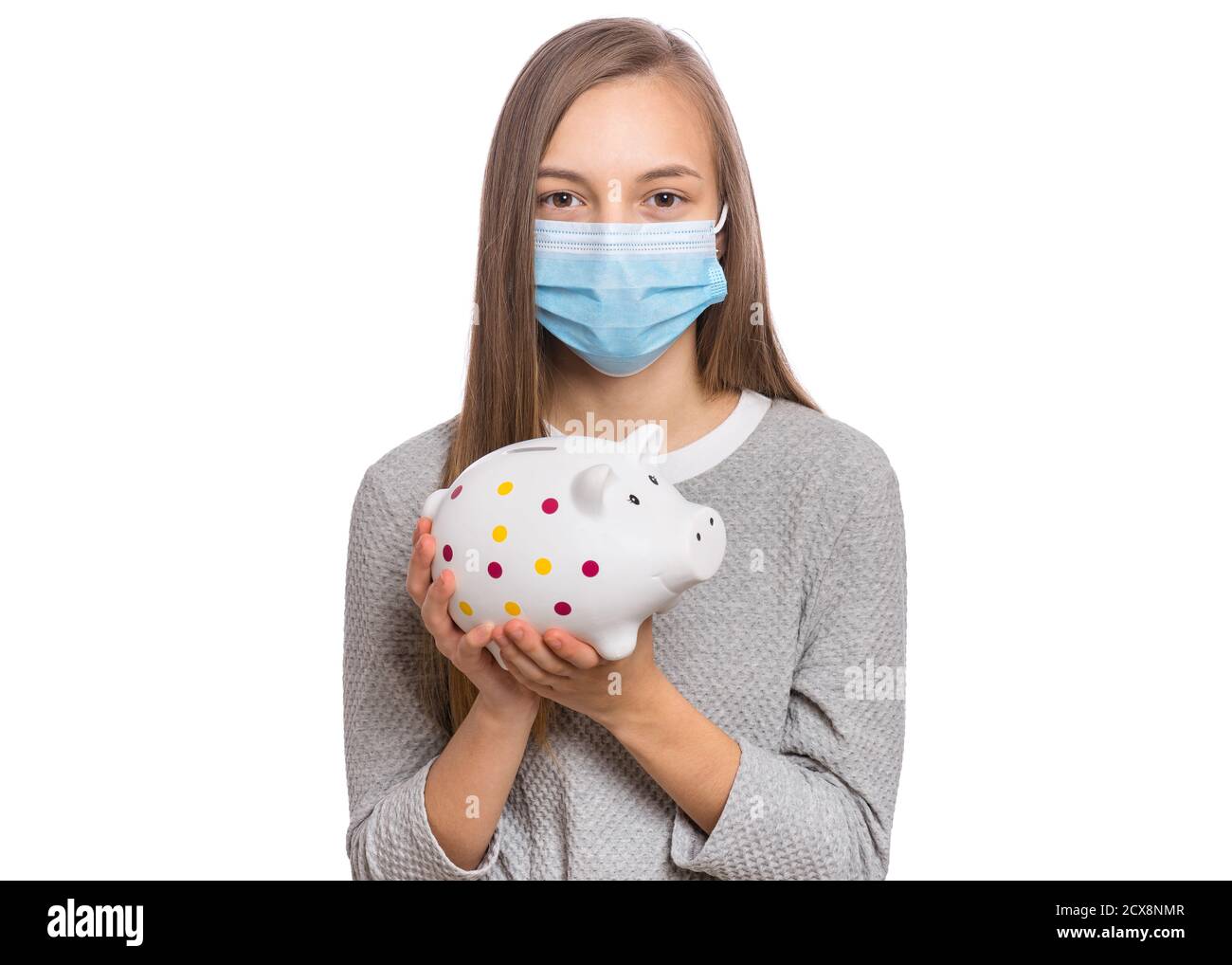 Concept of coronavirus quarantine. Portrait of teen girl wearing medical protective mask. Child holding Piggy Bank. Saving Money concept. COVID-19. Stock Photo