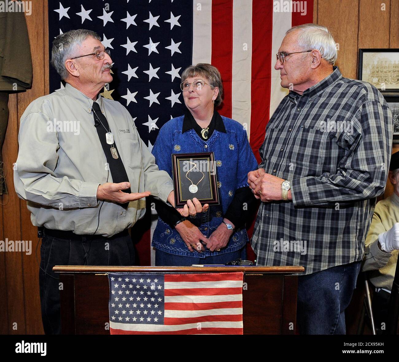 Retired U.S. Army Colonel Charles Rayl (L) presents Dale Potter (R) with  his father's lost World War I dog tag, as Potter's wife Dixie looks on,  during a ceremony in Cottonwood Falls,
