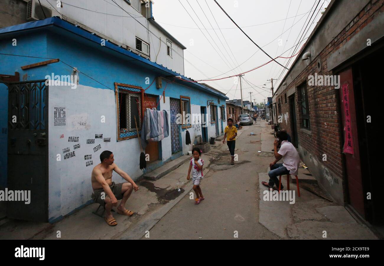 People sit in front of their houses at a residential area for migrant  workers in Beijing June 20, 2013. About 130 million Chinese migrants live  in tiny, sub-divided rooms rented out by