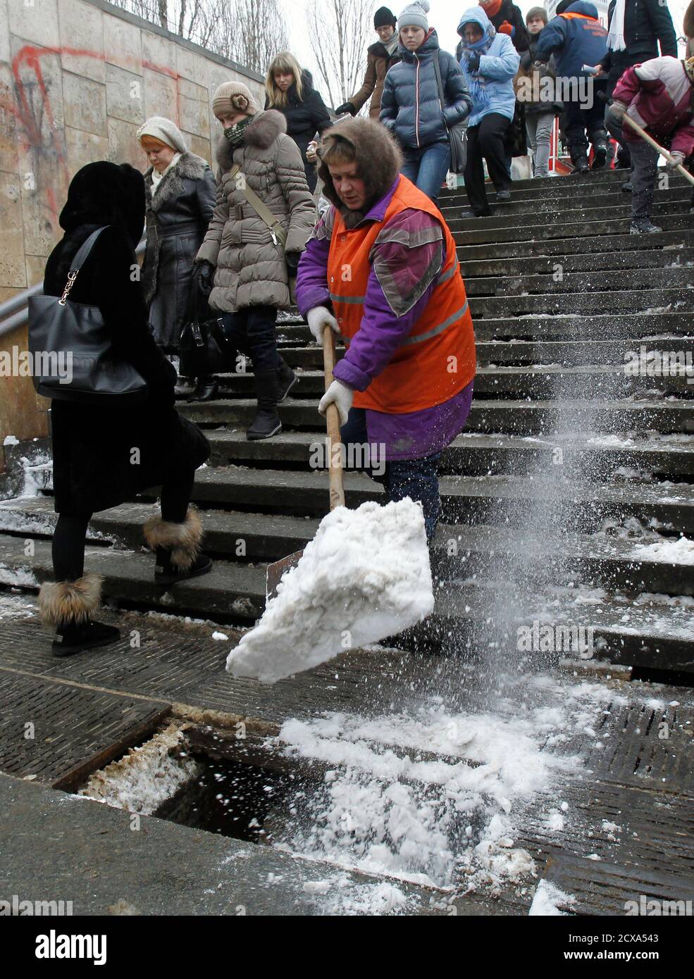 A woman removes snow from steps while people walk pass, as the air  temperature reaches about