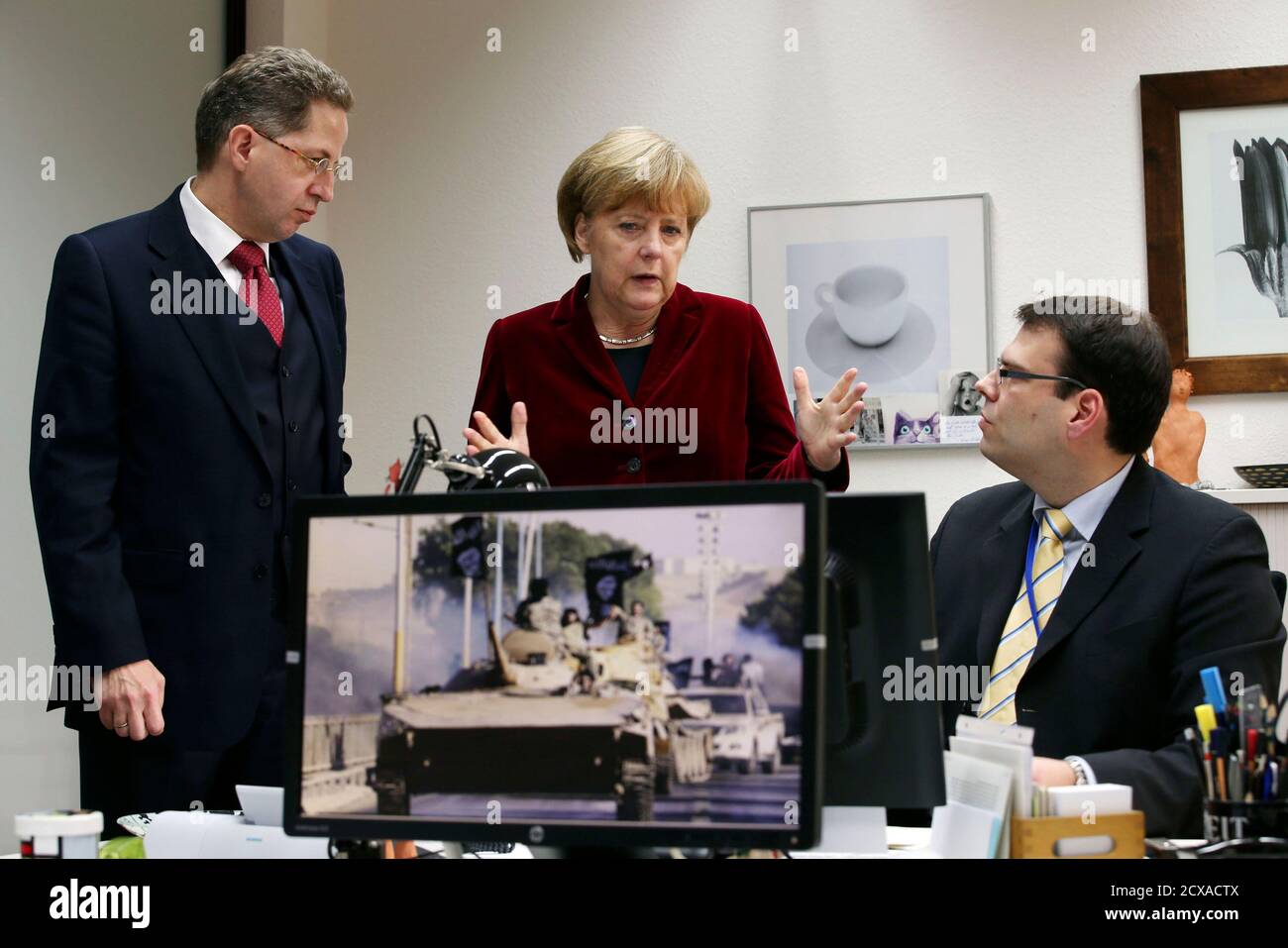German Chancellor Angela Merkel (C) and Hans-Georg Maassen (L), President of Germany's Bundesamt fuer Verfassungsschutz (BfV), the domestic intelligence service of the Federal Republic of Germany, talk to an agent of the BfV in Cologne October 31, 2014.  The agent is specialized in World Wide Web investigations of Islamic extremism. REUTERS/Oliver Berg/Pool (GERMANY - Tags: POLITICS) Stock Photo