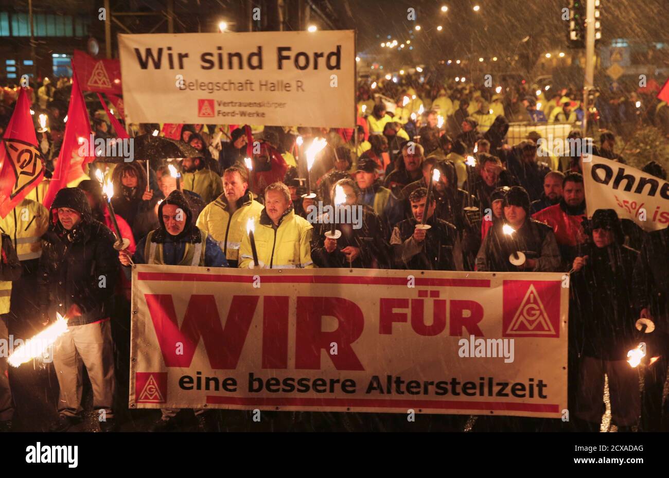 Snow falls as night shift workers of the Ford car factory in the Cologne suburb of Niehl, hold flaming torches during a temporary walkout for higher wages by Germany's engineering and metal workers union IG Metall early January 29, 2015. The union is demanding a 5.5 percent increase in salaries while employers have offered 2.2 percent. Any deal would have implications for wage negotiations in other German sectors and abroad. The banner in front reads 'We for better partial retirement', and the banner at rear reads 'We are Ford'. REUTERS/Wolfgang Rattay (GERMANY - Tags: TRANSPORT BUSINESS EMPLO Stock Photo