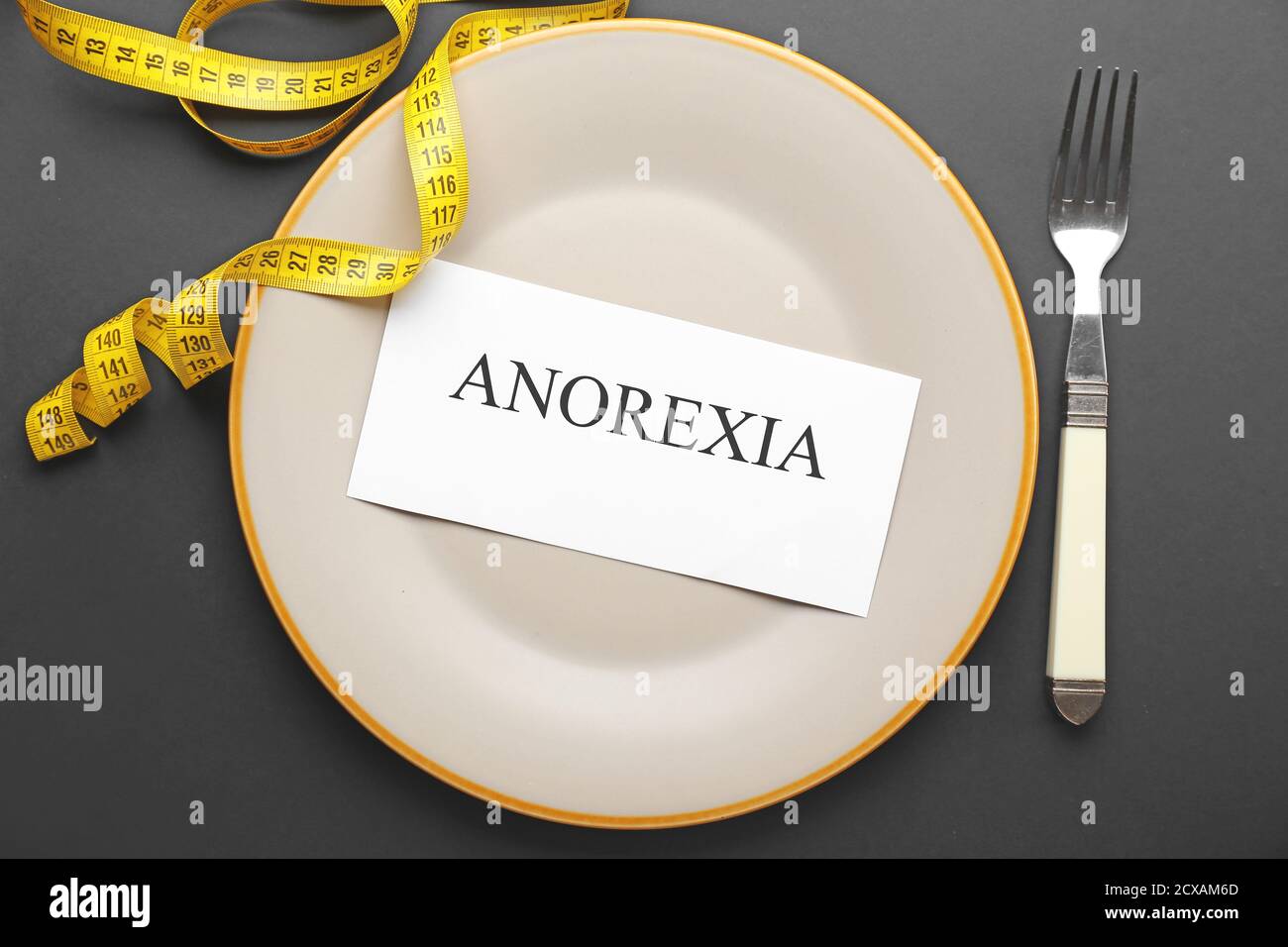 Plate with word ANOREXIA and measuring tape on dark background Stock Photo