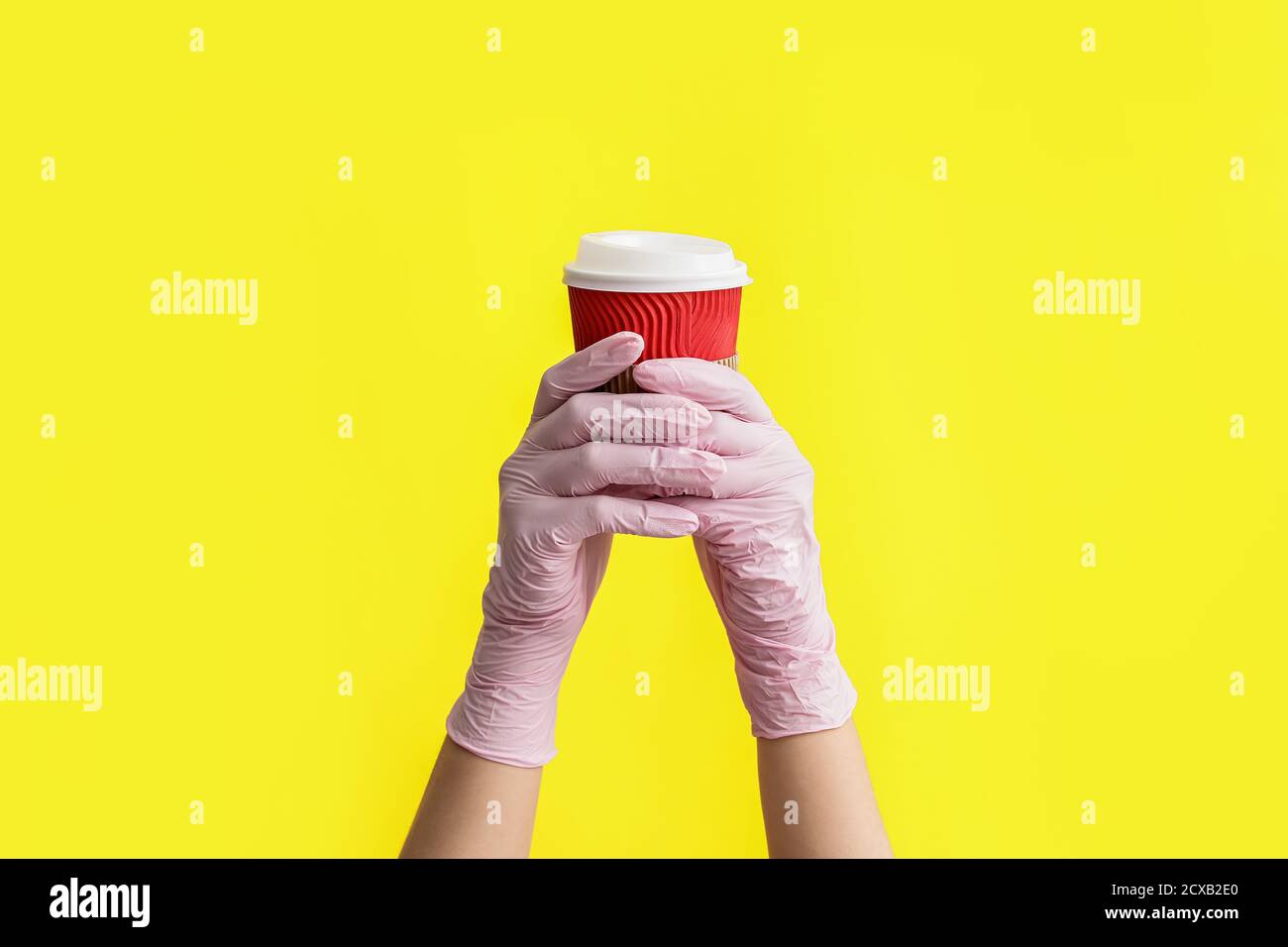 Hands in protective gloves and with cup of coffee on color background ...