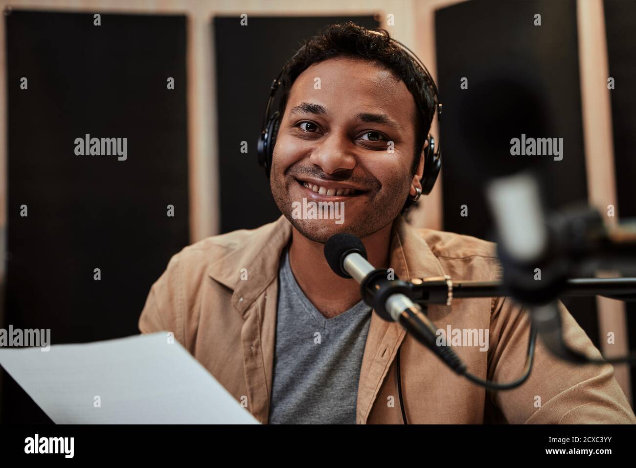 Portrait of happy young male radio host in headphones smiling at camera while talking, broadcasting in studio Stock Photo