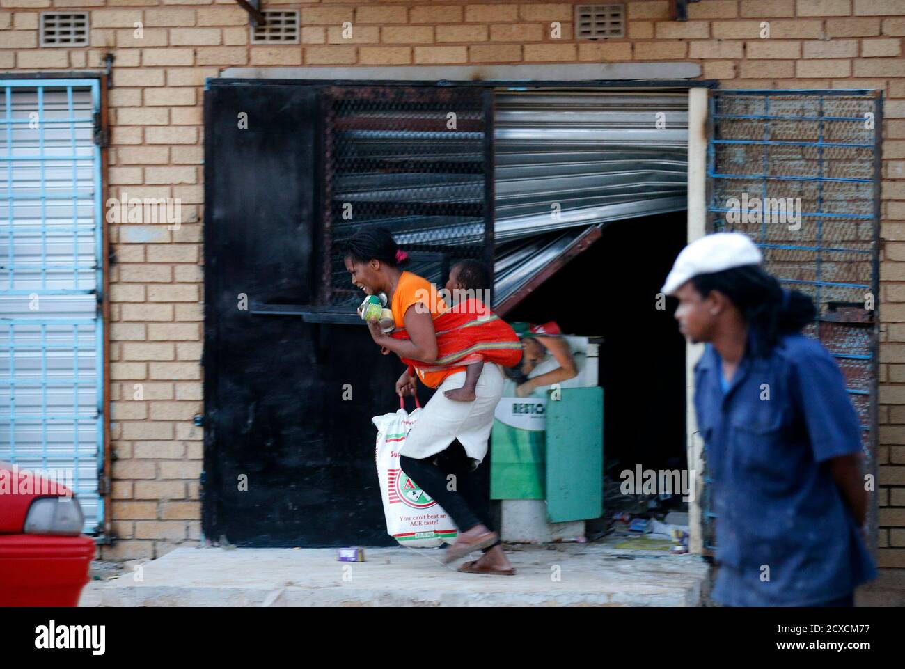 A Man Looks On As A Women With A Baby On Her Back Runs With Items From Shop Believed To Be Owned By A Foreigner In Soweto January 22 2015 Local Media