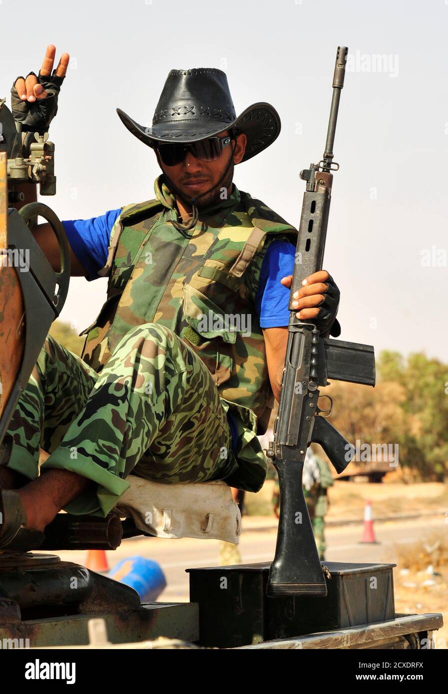 An anti-Gaddafi fighter holding his gun flashes the victory sign with his fingers at Khamseen Gate, 50 km east of Sirte September 25, 2011. Libyan interim government forces backed by NATO warplanes have mounted their deepest thrust into Muammar Gaddafi's home town of Sirte, getting as close as half a kilometre from the centre of the deposed leader's coastal stronghold. REUTERS/Esam Al-Fetori (LIBYA - Tags: POLITICS CIVIL UNREST CONFLICT) Stock Photo