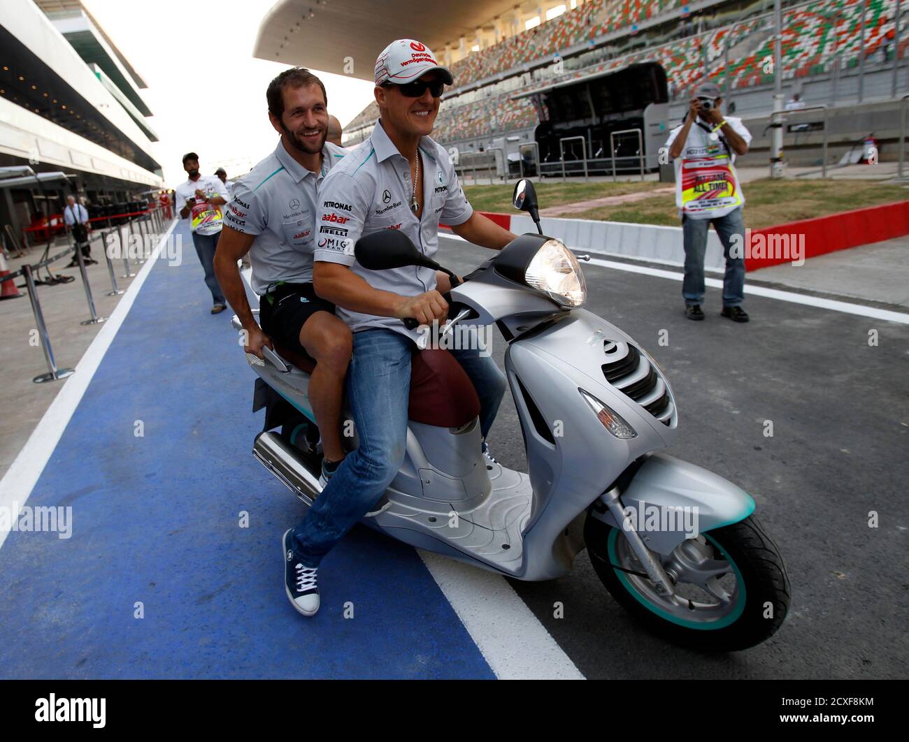 Mercedes Formula One driver Michael Schumacher of Germany and with a team  member ride on a scooter as they leave their pit to inspect the track at  the Buddh International Circuit in