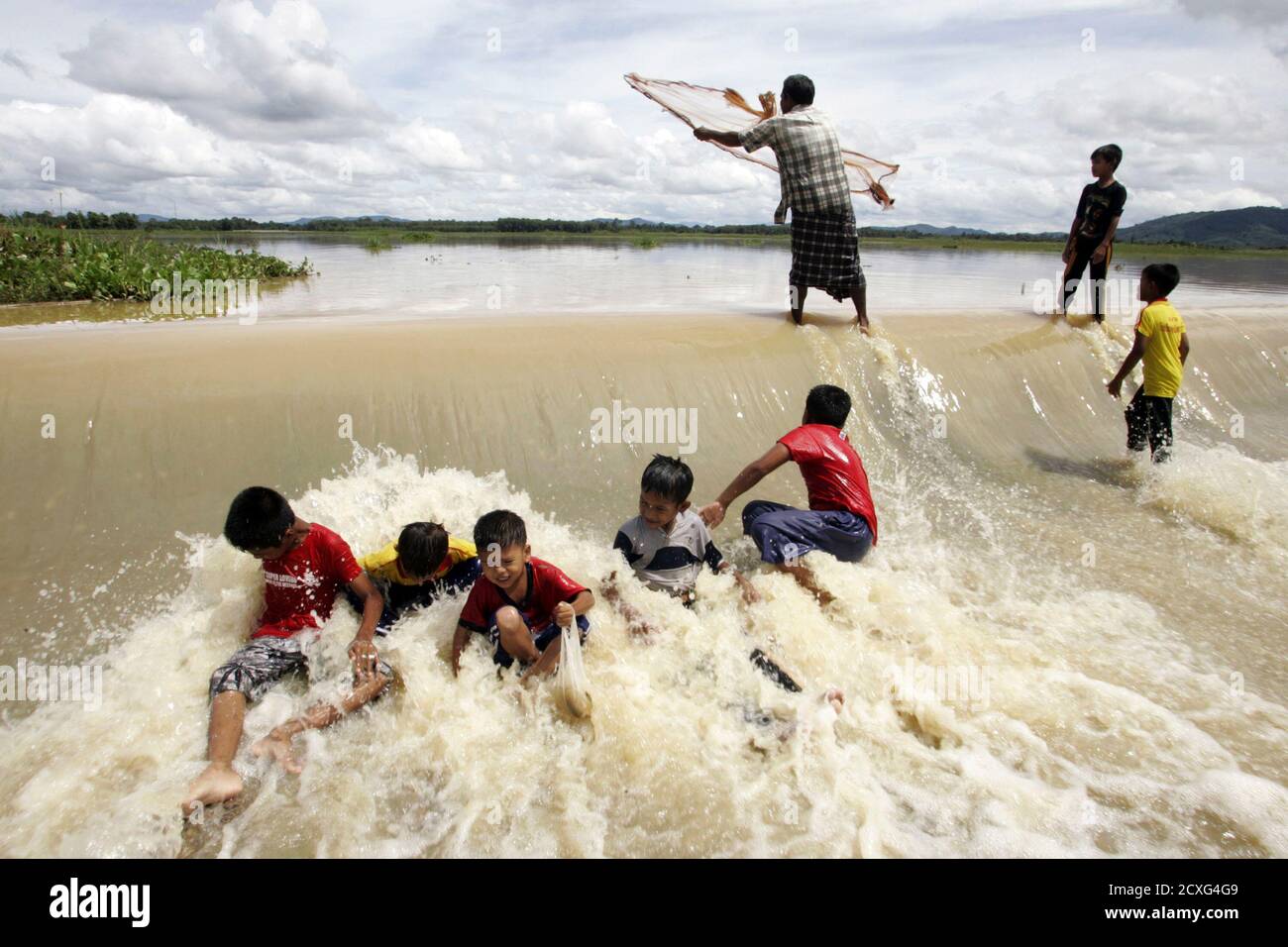 Children play in flood water as a man casts his fishing net in an area  affected by floods in Thailand's southern Pattani province November 2,  2010. Heavy rains drenched the main rubber
