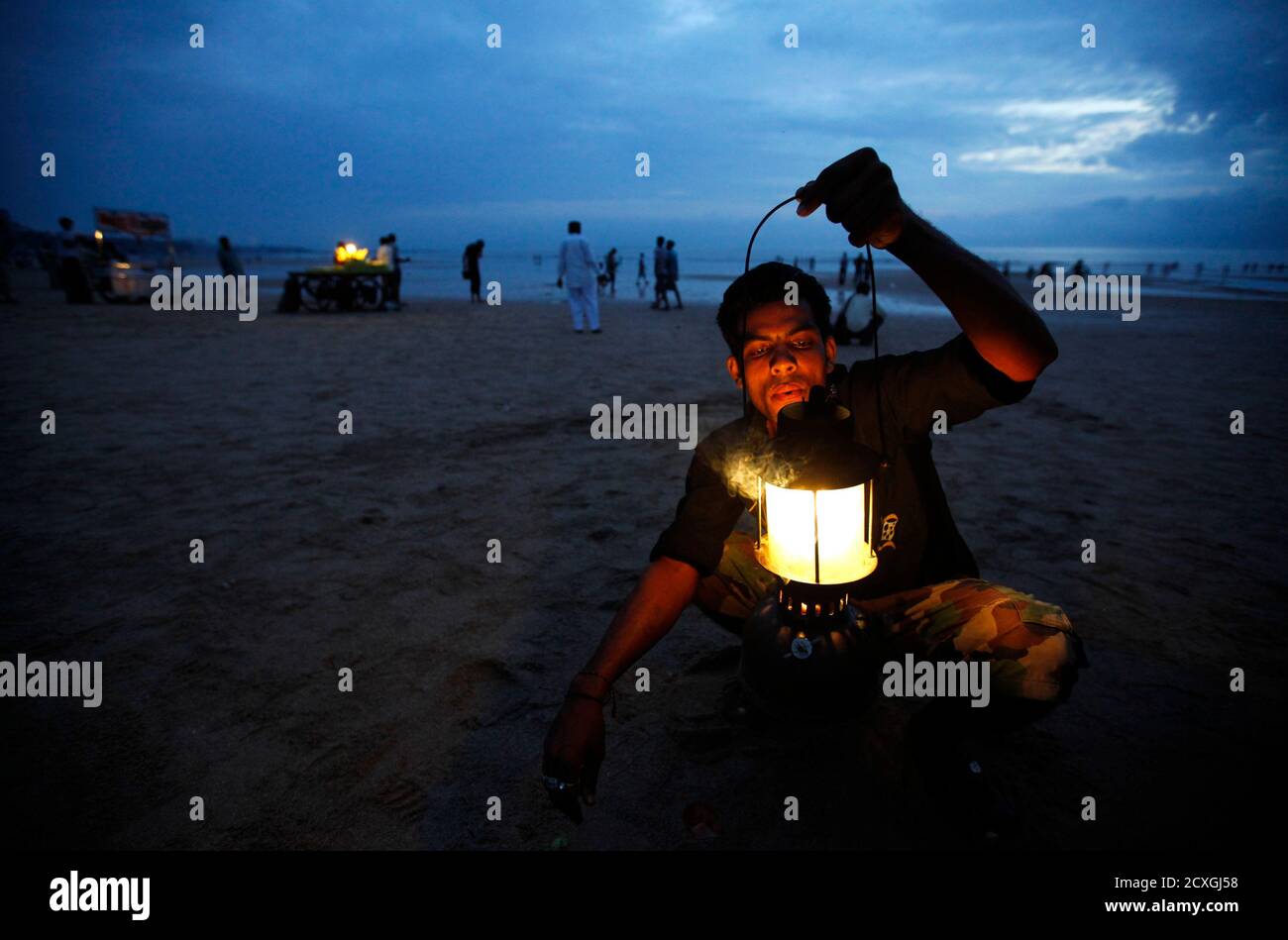 A street vendor lights a kerosene lamp for his food stall at a beach  against the backdrop of monsoon clouds in Mumbai August 27, 2010. India's  monsoon rains will be 15 percent