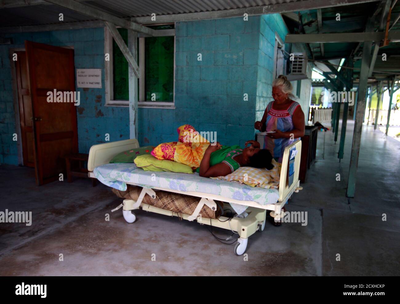 A woman prepares to feed a patient on a bed, placed outside due to lack of space, at the Nawerewere Hospital on South Tarawa in the central Pacific island nation of Kiribati May 25, 2013. Kiribati consists of a chain of 33 atolls and islands that stand just metres above sea level, spread over a huge expanse of otherwise empty ocean. With surrounding sea levels rising, Kiribati President Anote Tong has predicted his country will likely become uninhabitable in 30-60 years because of inundation and contamination of its freshwater supplies. Picture taken May 25, 2013.  REUTERS/David Gray     (KIRI Stock Photo