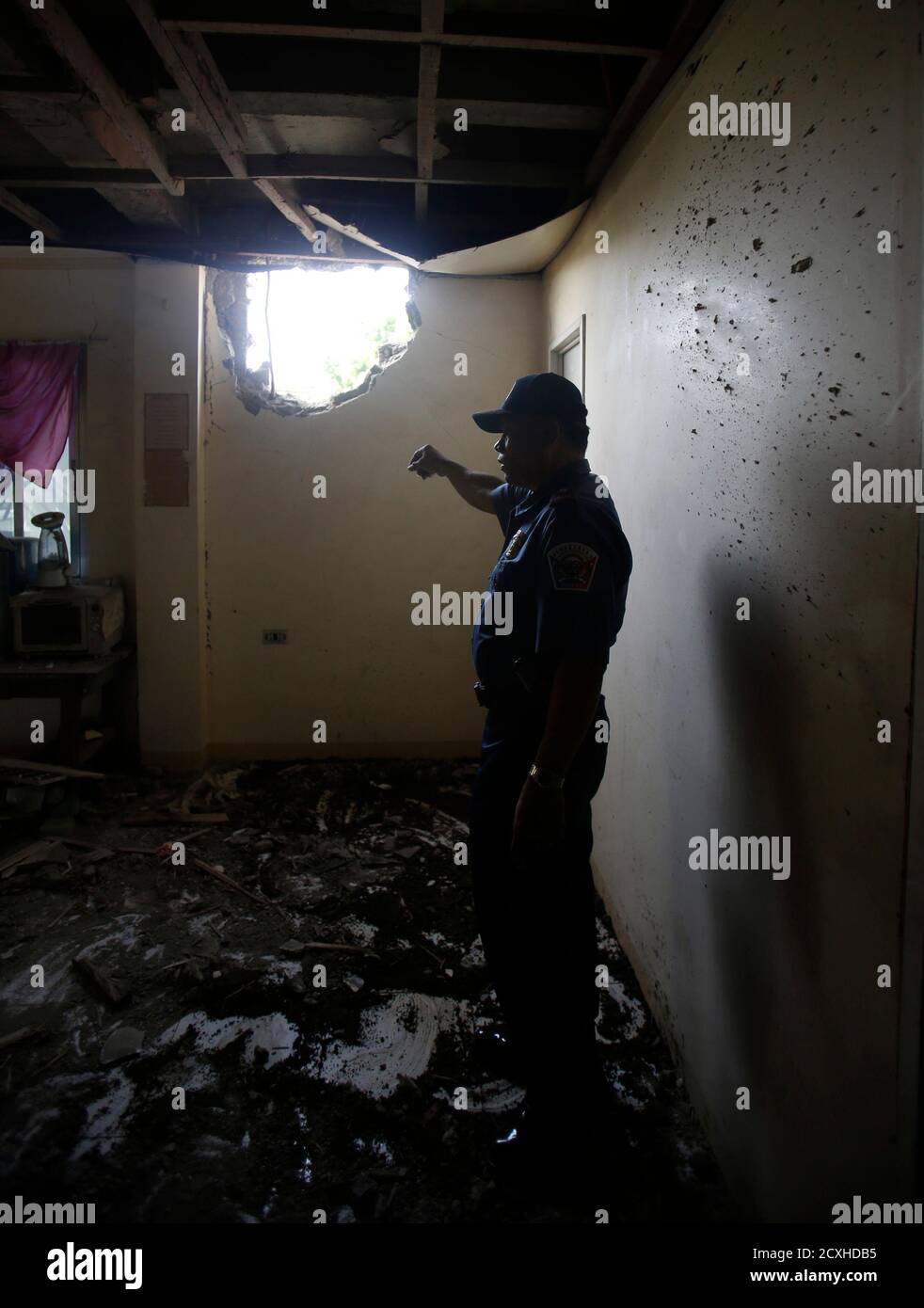 A policeman inspects a house damaged by a mortar round from Muslim rebels of Moro National Liberation Front (MNLF) positions, in Zamboanga city, southern Philippines September 21, 2013. Fighting between Philippine forces and Muslim rebels in in Zamboanga city has been confined to just two areas and should be over soon, President Benigno Aquino said on Thursday. According to a police spokesperson, the mortar round killed one individual. REUTERS/Erik De Castro (PHILIPPINES - Tags: CIVIL UNREST CONFLICT POLITICS) Stock Photo