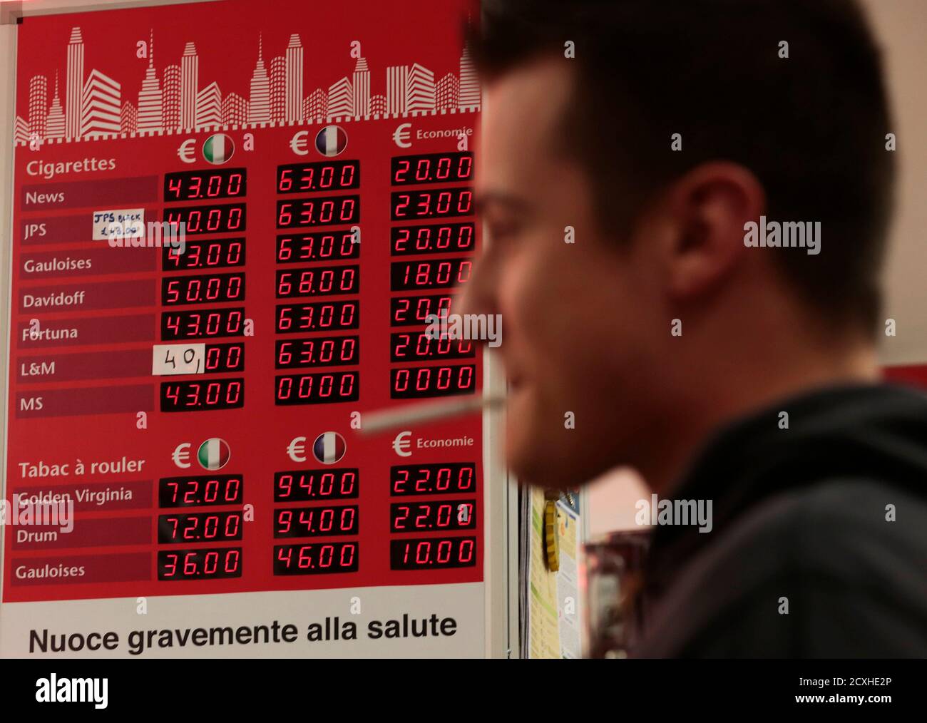 A French customer stands in front of an information board which displays the price of cigarettes when purchased in Italy (L) and France (C) with the difference in savings (R), in a supermarket in Latte, near the Franco-Italian border, January 13, 2014. The prices of cigarettes have increased by Euro 0.20 on January 13, 2014. REUTERS/Eric Gaillard   (ITALY- Tags: BUSINESS) Stock Photo