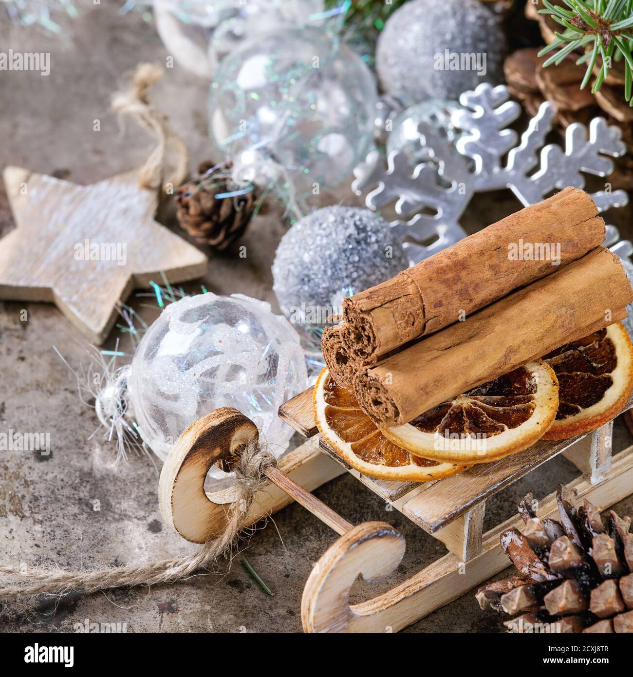 Christmas decoration card with glass and wooden toys, gift, cones and green tree over old dark metal background. Cinnamon on sled. Square image Stock Photo