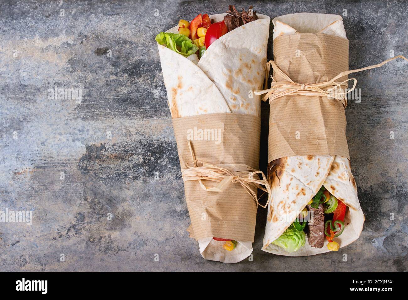 Mexican style dinner. Two papered tortillas burrito with beef and vegetables over old textured tin background. Flat lay with copy space Stock Photo