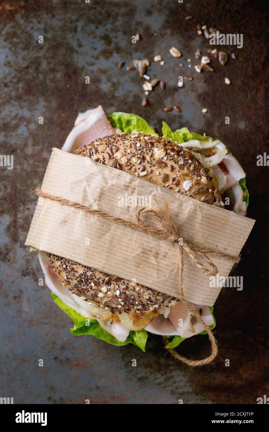 Papered Whole Grain bagel with fried onion, green salad and prosciutto ham over old rusty iron textured background. Top view Stock Photo