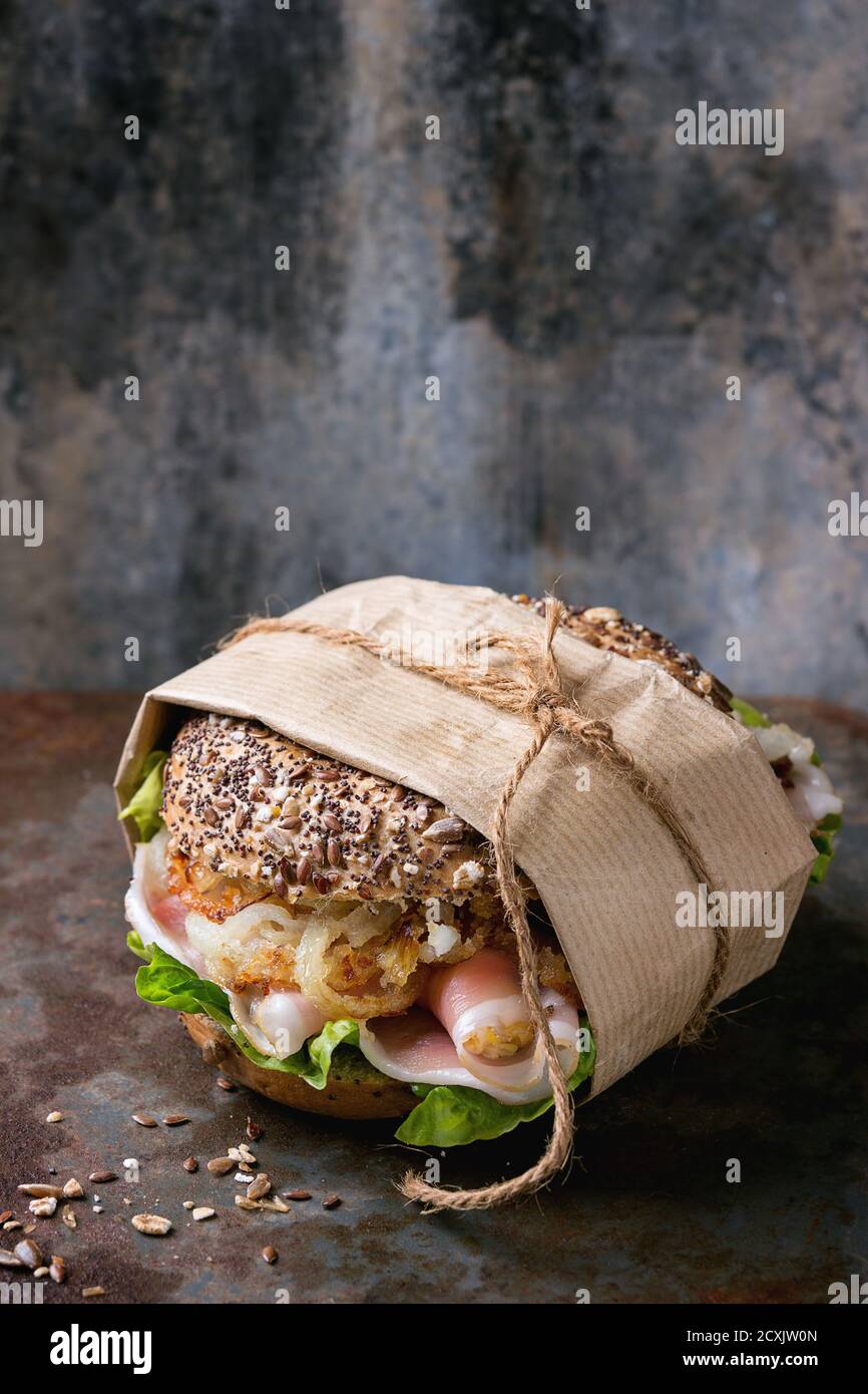 Papered Whole Grain bagel with fried onion, green salad and prosciutto ham over old rusty iron textured background. Stock Photo