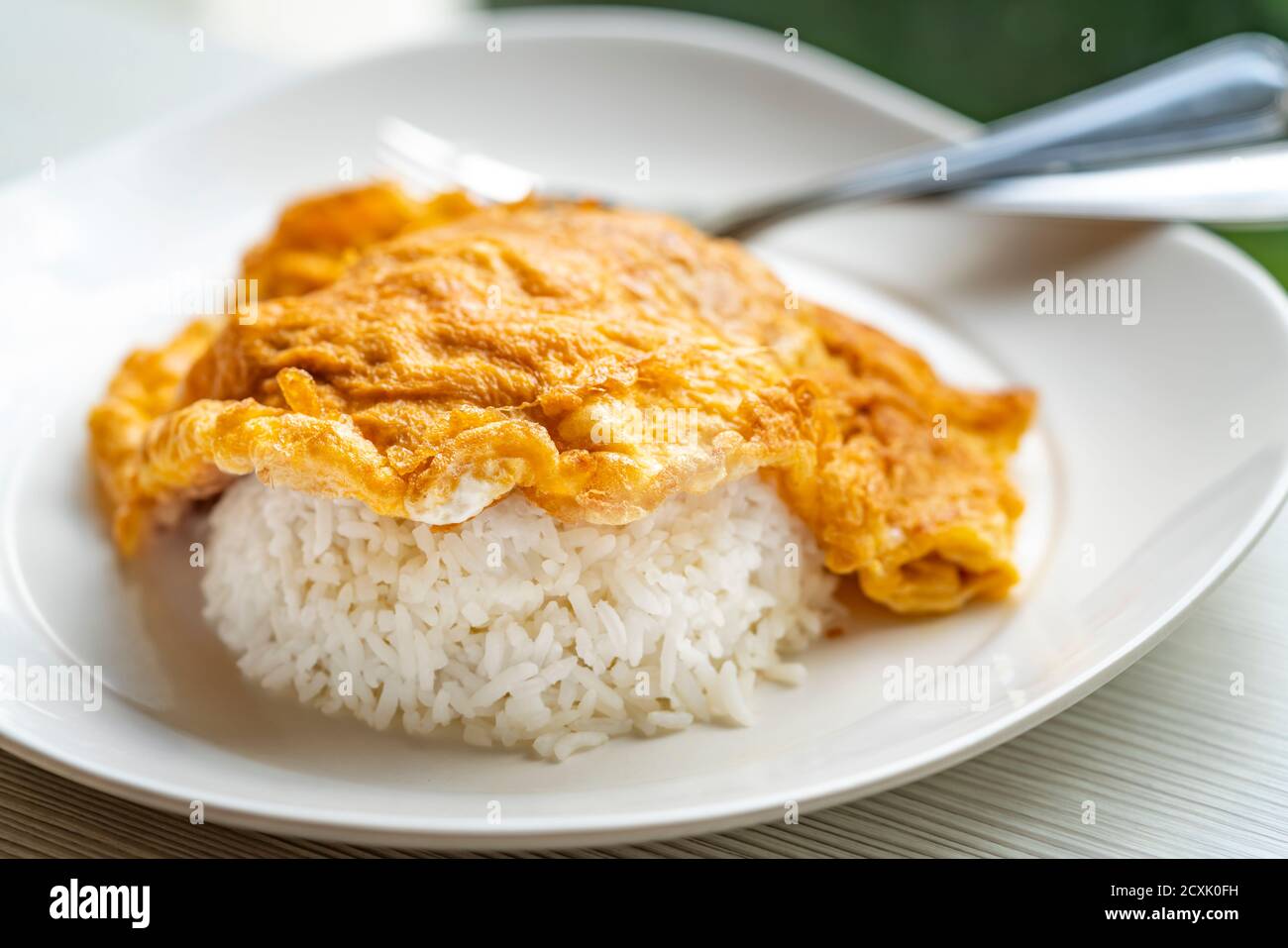 Easy Thai food menu, Thai omelette over rice or Kai Jeaw Rad Kow. Close up Thai omelette over white rice in white plate on table. Stock Photo