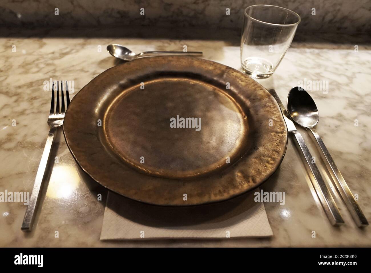 Close up black porcelain plate and stainless steel utensils arranged on marble bar table Stock Photo
