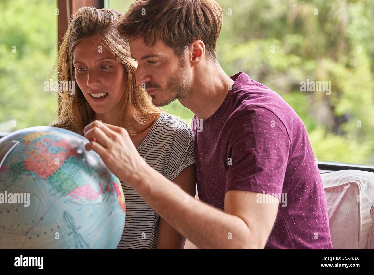 Young couple exploring world globe while sitting on sofa Stock Photo