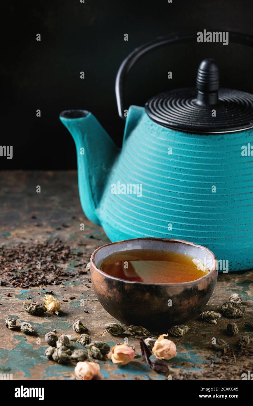 Turquoise iron teapot with ceramic cup of hot tea and variety of black