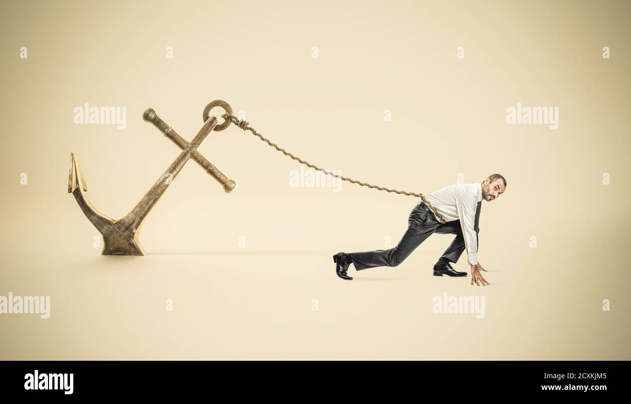 businessman in starting position tied to a big anchor fixed to the ground. Stock Photo