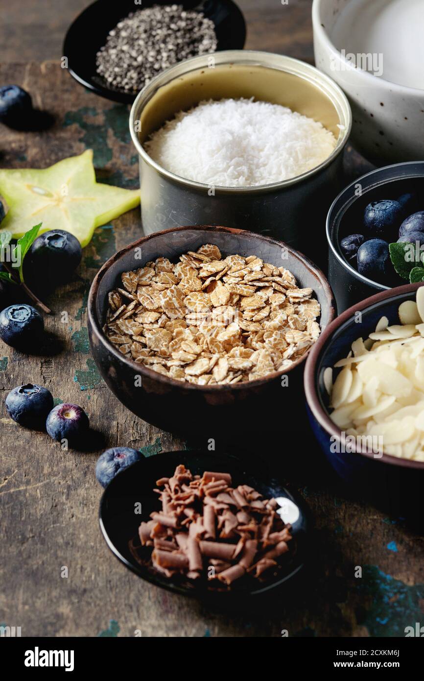 Ingredients for making smoothie for healthy breakfast. Bowls of yogurt, blueberries, granola, almond chia seeds, coconut, milk, chocolate, mint, caram Stock Photo