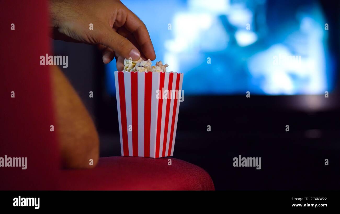 Eating popcorn while watching a movie on the couch at home. Scene in a house with bright lights, a movie night with the scent of pop corn. Stock Photo