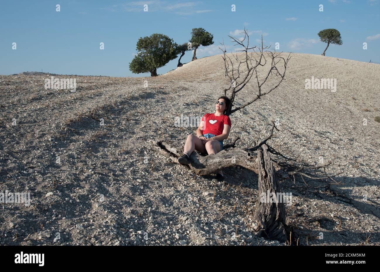 Young woman sitting on a dry tree log in the desert hill. Dry land no water. Nicosia Cyprus Stock Photo