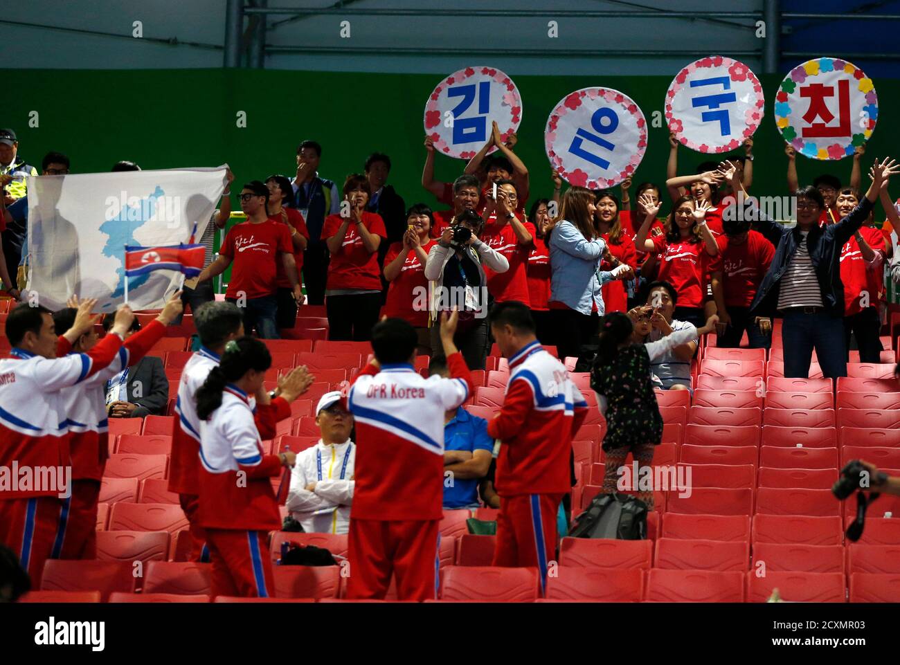 North Korean (bottom) and South Korean spectators, the latter holding a map of North and South Korea as one land mass, sing songs and wave flags at each other after North Korea's Kim Un Guk broke his second world record of the night and won a gold medal for the men's 62kg weightlifting competition at the Moonlight Garden Venue during the 17th Asian Games in Incheon September 21, 2014. Kim became the second North Korean weightlifter in two days to break world records at the Asian Games, lifting 154kg in the snatch component of the men's 62kg category on Sunday before setting a new mark for his  Stock Photo