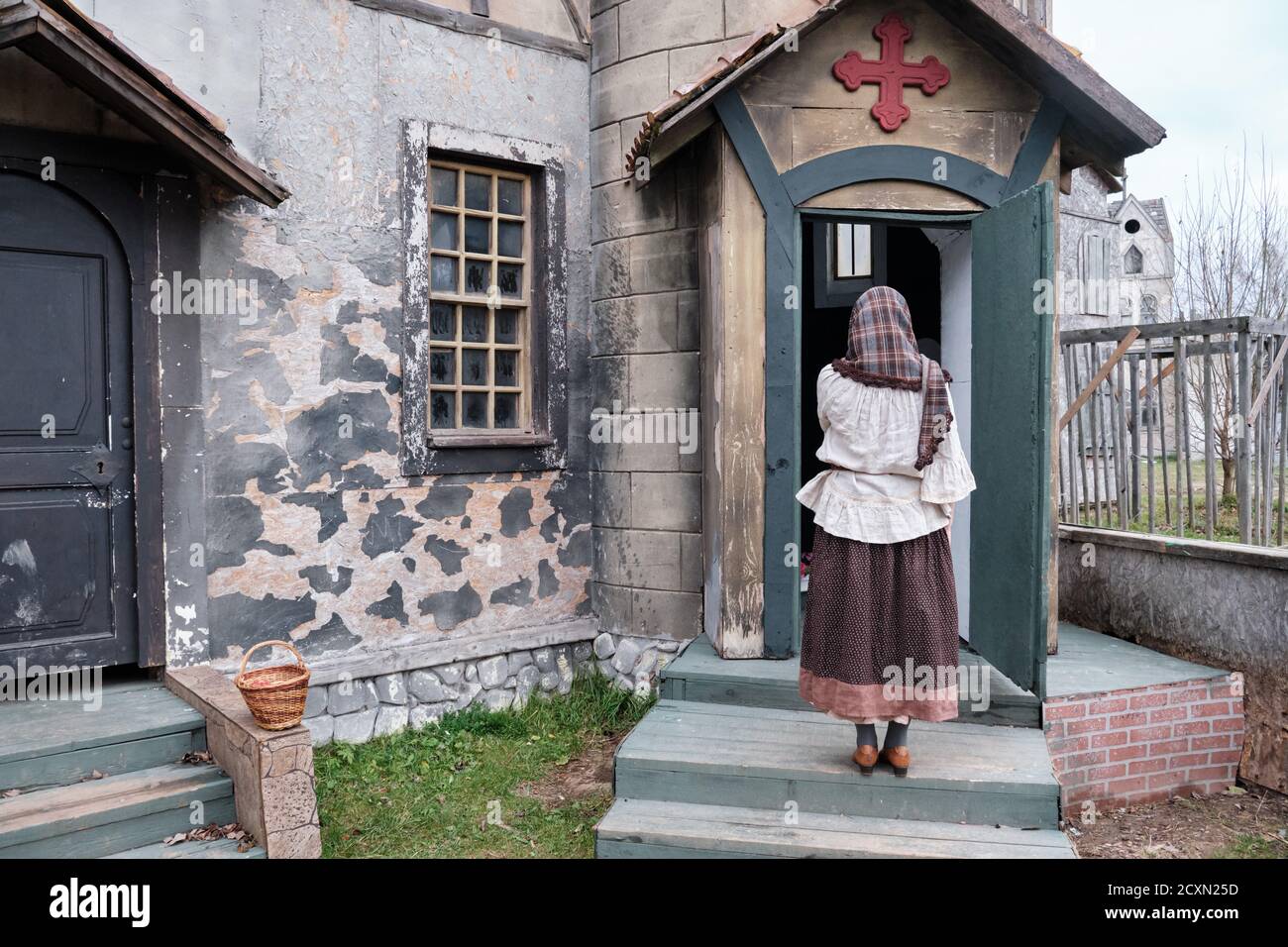 Young woman parishioner stands with her back and prays at the door of a medieval church. Halloween gothic vintage costume Stock Photo
