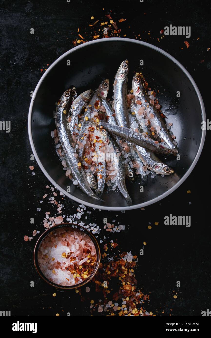 Lot of raw fresh anchovies fishes in black ceramic bowl with chili