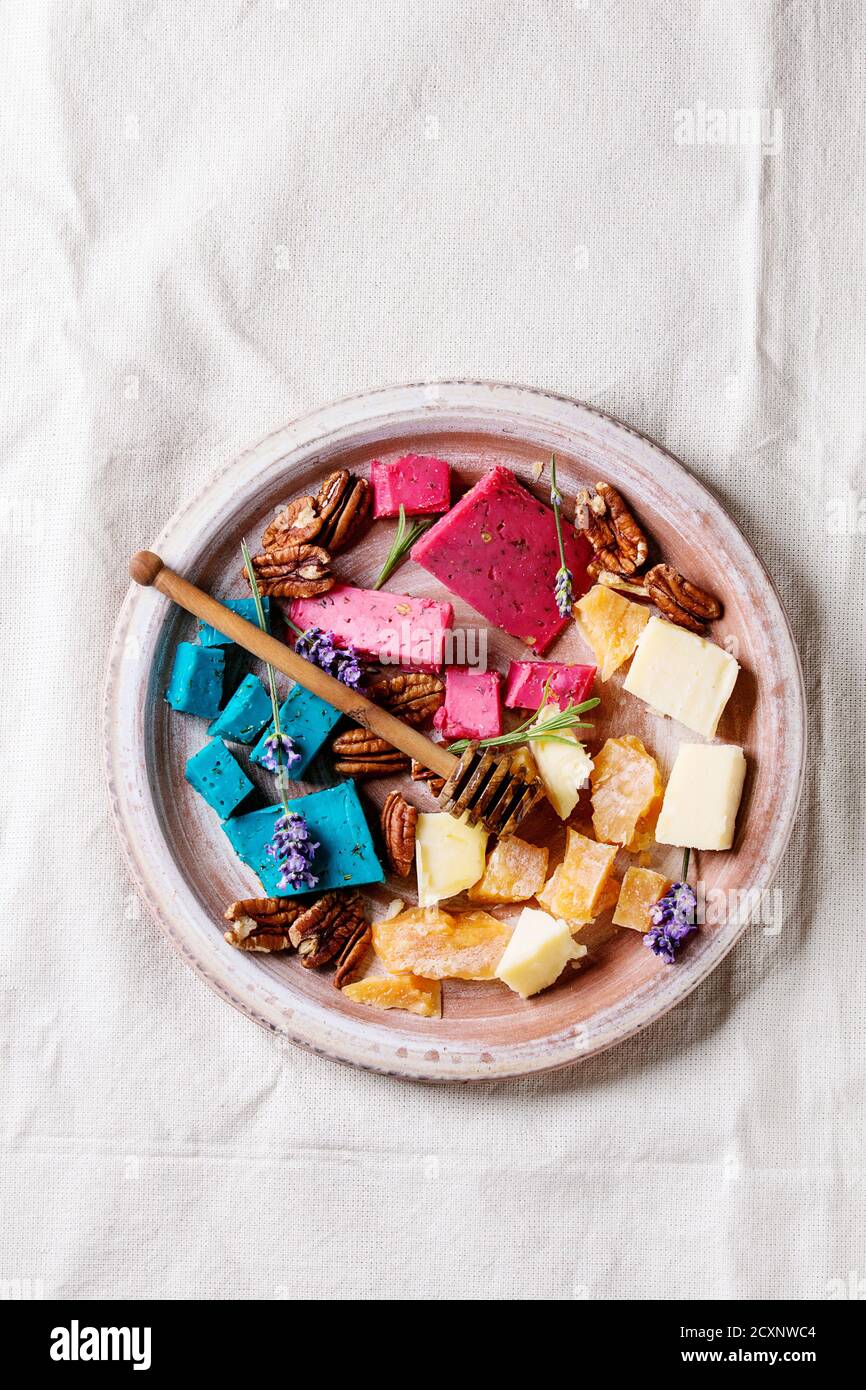 Variety of colorful holland cheese traditional soft, old, pink basil, blue lavender served with pecan nuts, honey, lavender flowers on terracotta plat Stock Photo