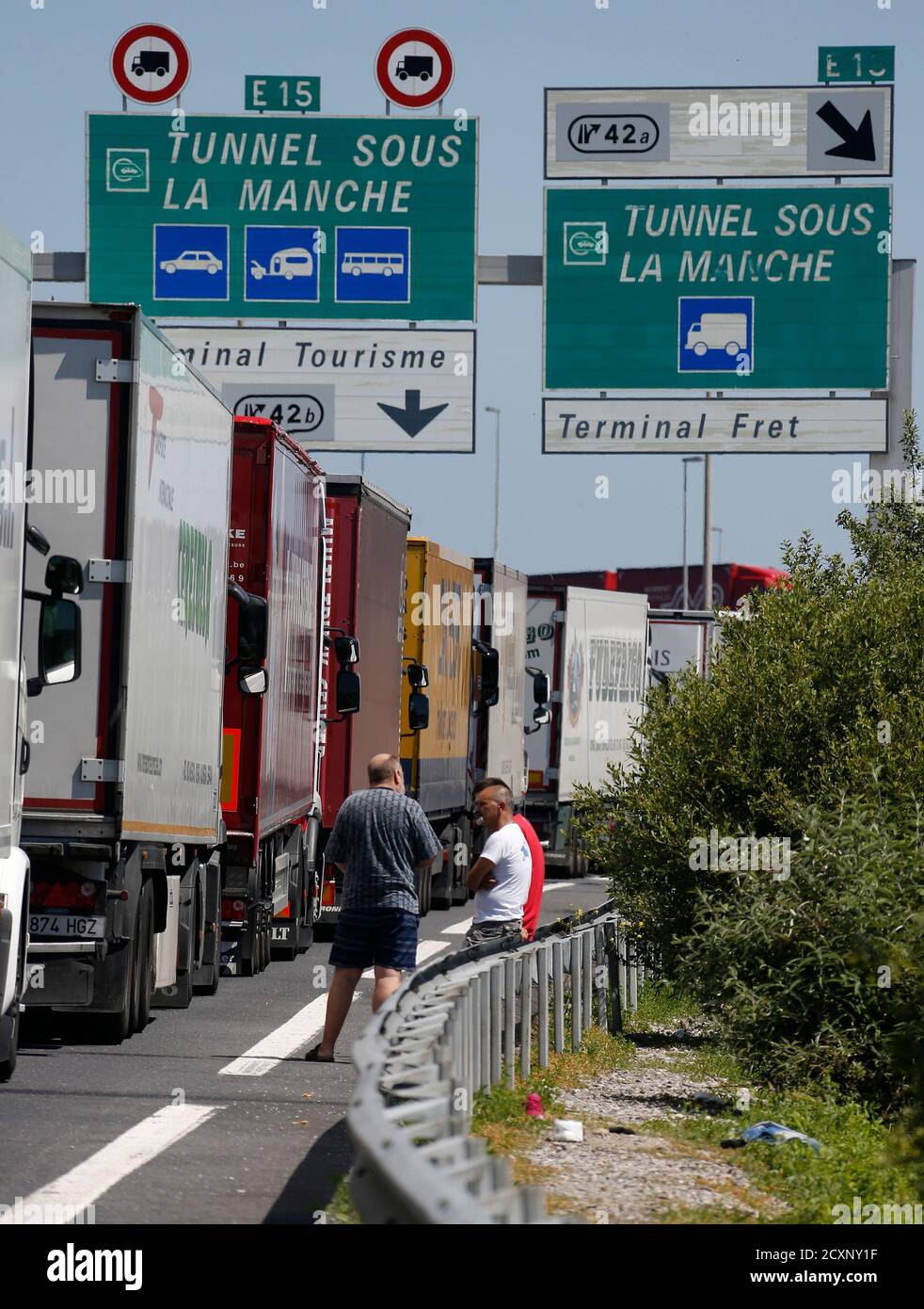 Truck drivers wait near their lorries blocked on a road which leads to the Channel  Tunnel terminal in Coquelles near Calais, northern France, June 30, 2015.  The Channel Tunnel closed again on