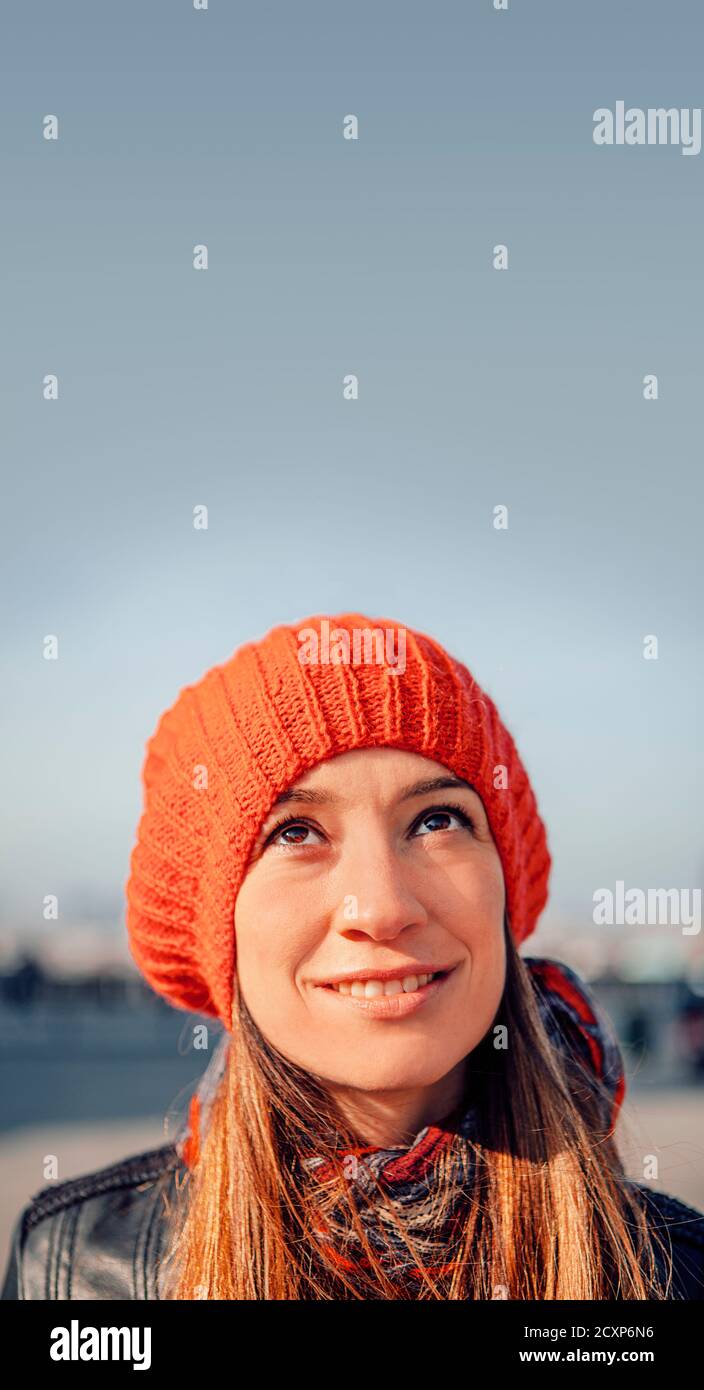 portrait of a naturally beautiful woman wearing a red knit hat smiling and looking up to a clear sky above her - real people and real life moment Stock Photo