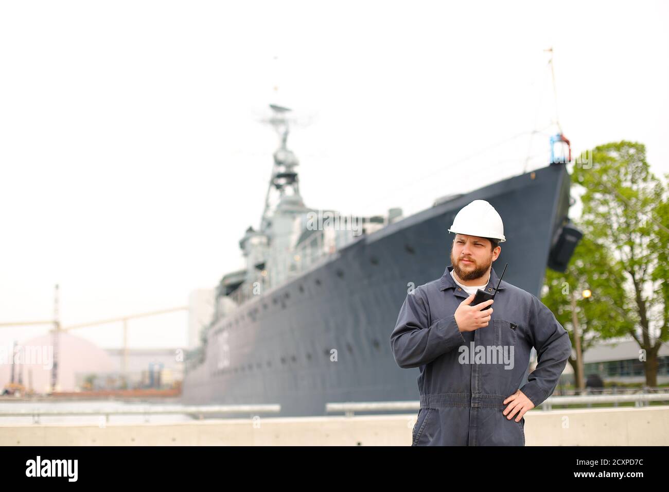 Marine chief mate talking by walkie talkie radio and standing near offshore vessel in bakground. Stock Photo