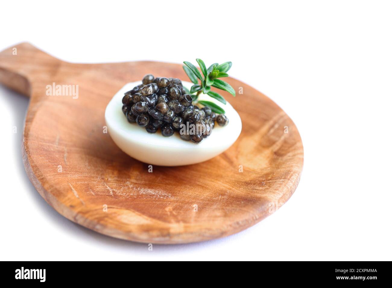Gourmet dish, delicious black sturgeon caviar on a quail egg with rosemary on the wooden plate isolated on the white background Stock Photo