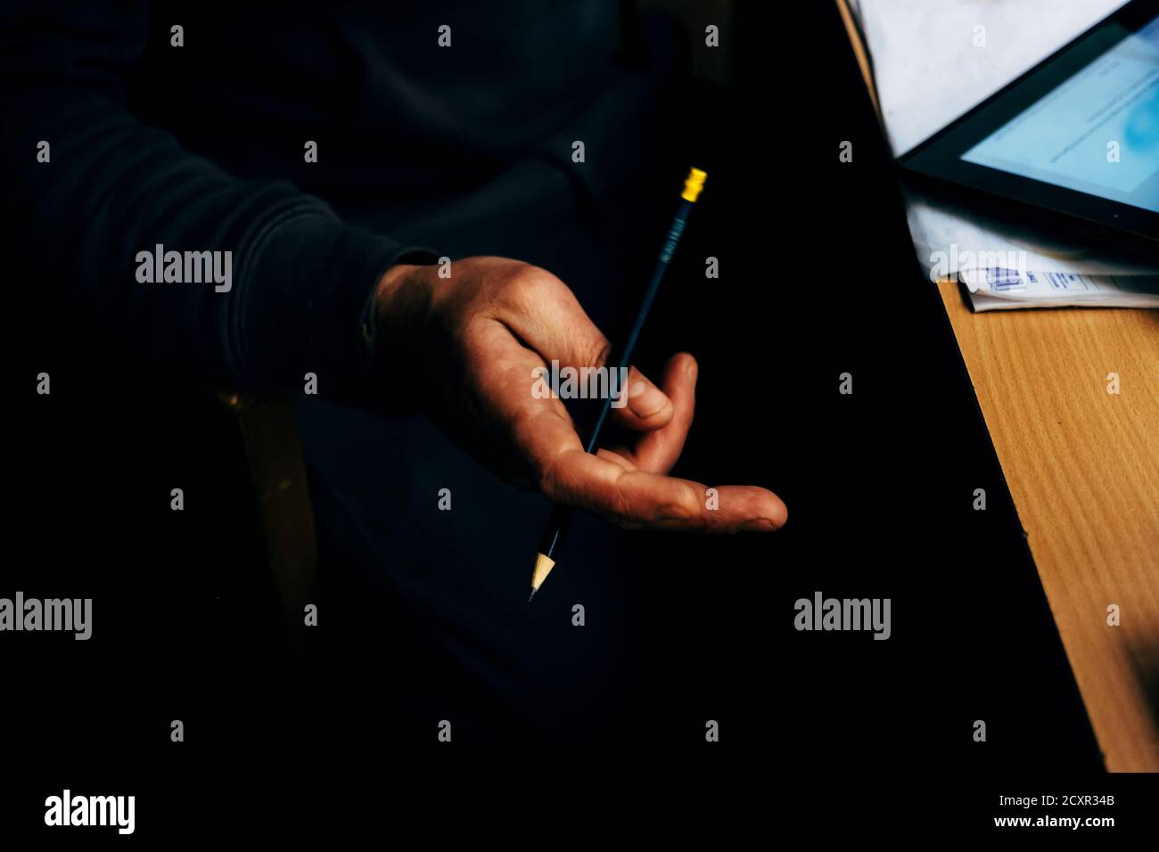 detail of the hand of a man holding and wrapping a pencil around the fingers while he is busy at the office desk Stock Photo