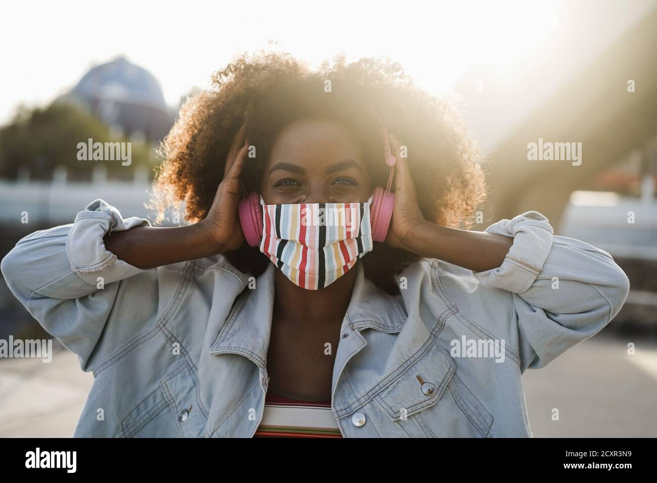 Black girl listening music with headphones while wearing face mask outdoor - Coronavirus lifestyle concept Stock Photo